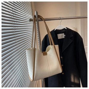 Detail of minimalist cream leather tote bag with brown trim hanging on metal hanger