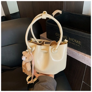 Detail of cream pleated bucket bag with drawstring closure and cute teddy bear charm