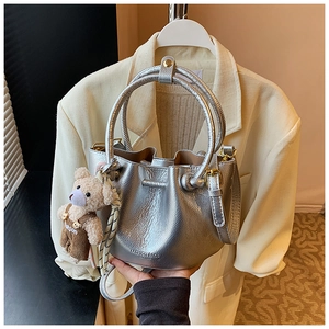 Detail of silver metallic bucket bag with leather texture and cute bear pendant charm