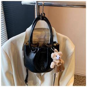 Glossy black bucket bag detail with a cute teddy bear charm hanging from the strap