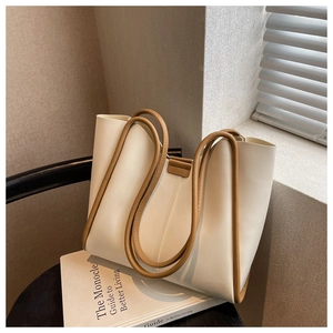 Detail of cream faux leather tote bag with dark brown contrast piping on a chair