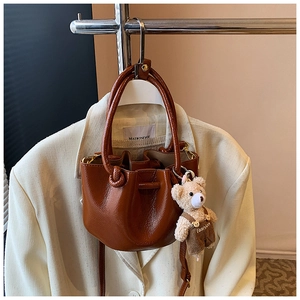 Detail of dark brown bucket bag with lychee texture and cute teddy bear charm