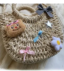 Détail du sac en paille tissé à la main avec breloque ours et nœuds décoratifs colorés