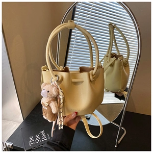Detail view of beige pleated bucket bag with round handle and bear pendant in a mirror