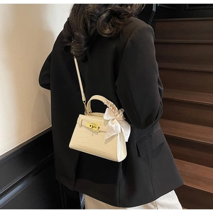 Détail du sac à main beige texture crocodile avec fermoir doré et nœud en soie