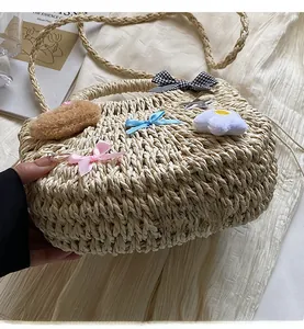 Détail du sac en paille tressée avec nœuds colorés, breloque en peluche et bandoulière