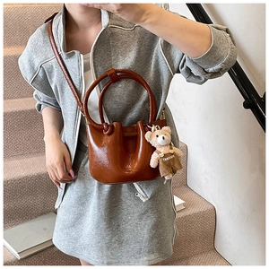 Detailed shot of brown glossy bucket bag with round handle and cute bear charm pendant