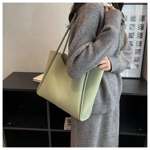 Light green large tote bag with shoulder straps shown on model in a modern indoor setting