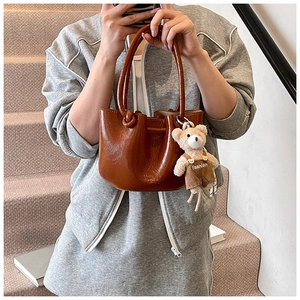 Detail of a brown glossy bucket bag with pleated texture and a cute bear bag charm