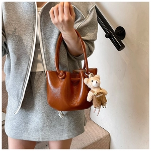 Detail of dark brown glossy leather bucket bag with a cute teddy bear charm on the side