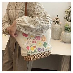 Dettaglio della borsa tote in tela con stampe floreali e base in paglia sulla spalla di un modello