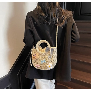 Détail d'un sac en paille tissé à la main avec décor floral et breloque ours sur modèle