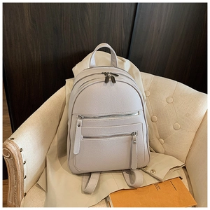 Detail of grey lychee leather backpack with silver zippers on a beige fabric sofa