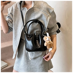 Detail of black glossy bucket bag with round handles, pleated top and cute bear pendant