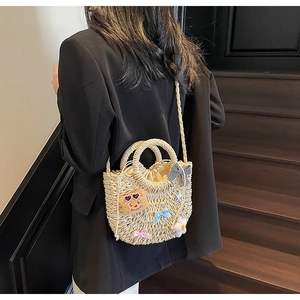 Détail du sac en paille beige tissé avec des écussons ours et fermeture par cordon