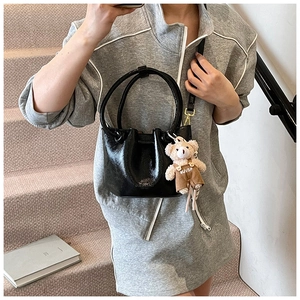 Close-up of black glossy pleated bucket bag with a cute brown teddy bear pendant detail