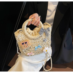 Détail du sac en paille avec décor floral, rubans et accessoire en peluche mignon