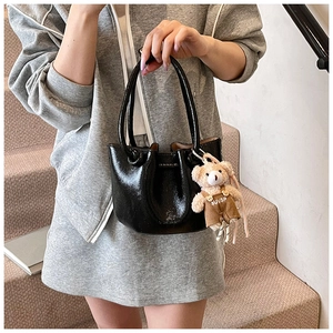 Detail of glossy black patent leather bucket bag with a cute teddy bear charm pendant