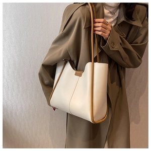 Close-up of minimalist cream tote bag with brown edges worn on shoulder with a trench coat