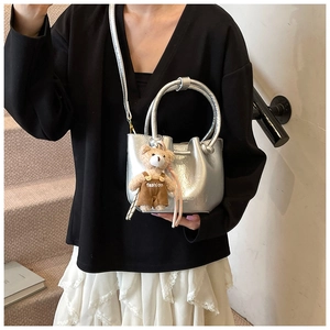 Silver metallic mini bucket bag with plush bear charm worn by model on stairs
