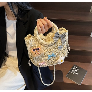 Détail du sac en paille avec ours en peluche, nœuds colorés et fleurs de marguerite