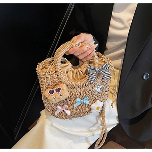 Détail du sac en paille tressé à la main avec un nœud vichy et un charm d'ours mignon