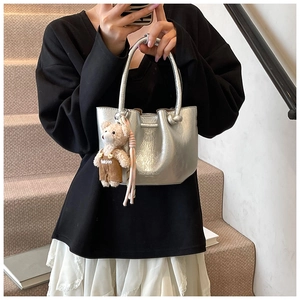 Silver metallic bucket bag with knotted handle and plush bear charm on a female model