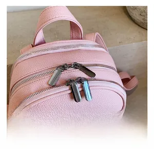 Close-up of pink litchi grain leather backpack with dual gunmetal zippers and precise stitching