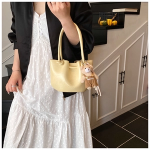 Detail of creamy yellow pleated bucket bag with a cute teddy bear fashion charm