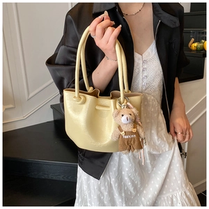 Detail of yellow pleated bucket bag with bear pendant and fashion bags embossed text