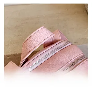 Detail of pink lychee leather backpack showing top handle and smooth metal zippers