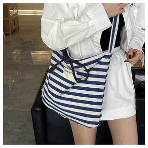 Detail of striped canvas tote bag featuring a black bow and branded woven label