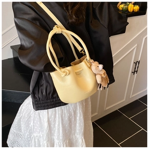 Detail of cream pleated bucket bag with drawstring closure and cute teddy bear charm