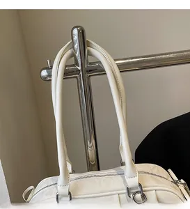 Detail of white leather shoulder bag featuring round long straps and smooth top zipper