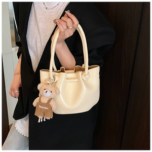 Detail of cream pleated bucket bag with knot handle and teddy bear charm accessory