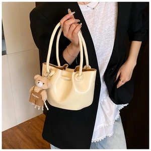 Detail of cream pleated bucket bag with knot handle and brown teddy bear charm