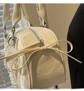 Detail view of smooth zipper and pleated leather bow on a cream bowling handbag