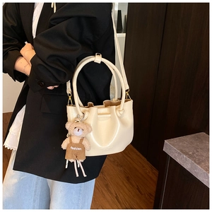 Detail of cream white pleated bucket bag featuring a cute teddy bear charm and strap