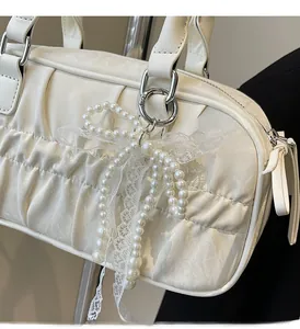 Close-up of white pearl bow pendant with lace detail on a leather shoulder bag