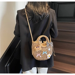Détail du sac en paille tissé beige avec breloque d'ours en peluche et nœuds en soie
