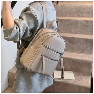 Detail view of khaki pebbled leather backpack with multiple functional zip pockets