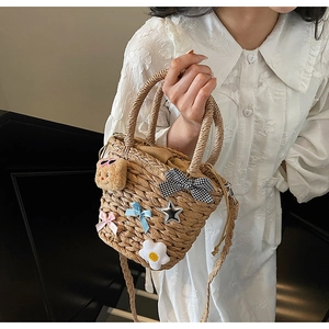 Détail d'un sac seau en paille avec breloques d'ours et nœuds sur robe en dentelle