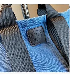 Détail du tissu denim bleu, sangle en nylon noir et logo en cuir sur le sac fourre-tout