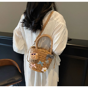 Détail d'un sac seau en paille tissée orné d'un ours mignon et de nœuds en peluche