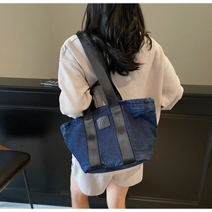 Détail d'un grand sac cabas en denim avec large bandoulière et écusson en cuir