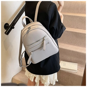Side view of a light grey pebbled leather backpack showing its compact texture and zippers
