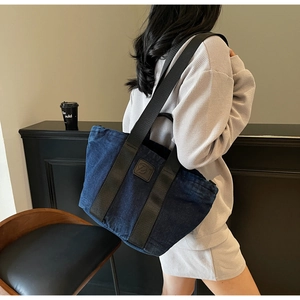 Détail du sac cabas en denim bleu foncé avec sangles noires et logo en cuir