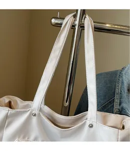Detail of wide shoulder straps and metal rivet accents on a minimalist white canvas tote