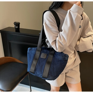 Détail d'un grand sac cabas en jean avec écusson en cuir et bandoulière noire