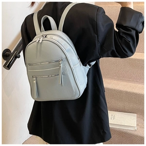 Detail view of a stylish grey-blue PU leather backpack with multi-zipper layers on a model